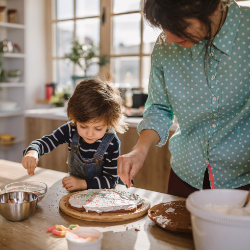 A mom and her young child decorating a cake in a modern kitchen.