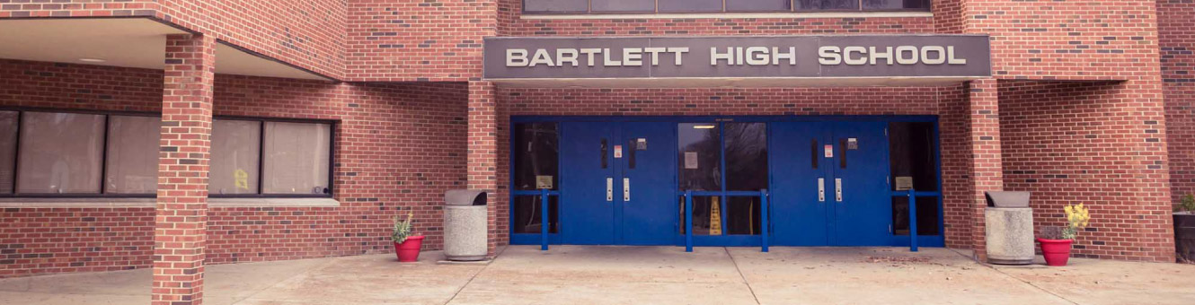 The front of a large brick building with blue doors. Text above the doors read, "Bartlett High School"