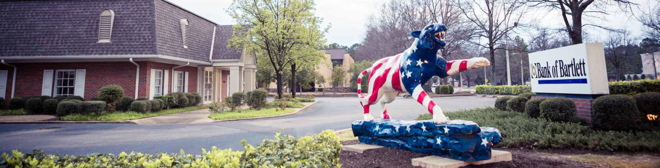 Outside shot of a Bank of Bartlett location. There is a red, white, and blue tiger sculpture in the foreground.