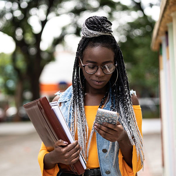 Young woman holding school supplies and looking at her phone