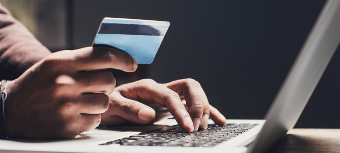 Close up of a person's hands, one is holding a credit card while the other is typing on a laptop keyboard