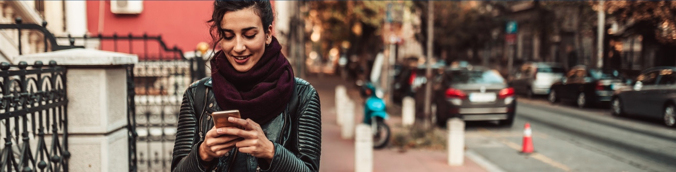 Young woman walking down a sidewalk and looking down at her phone.