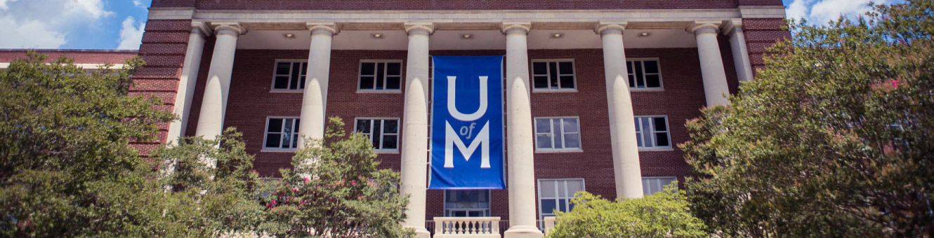 Wide shot of an old building with a blue banner on the outside that says "U of M"