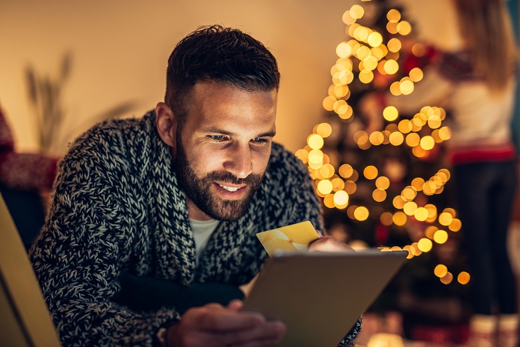 man holding card and tablet in front of a christmas tree