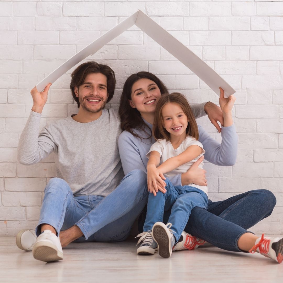 smiling family of three under a board intended to represent a house